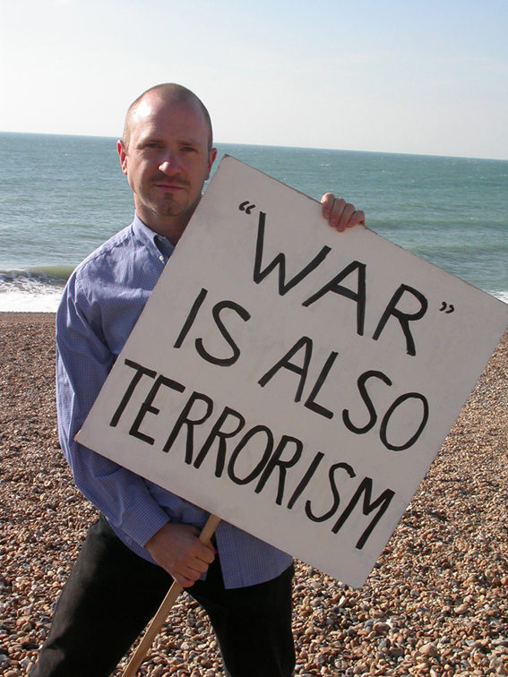 Michael Nendick holding a placard that reads "War is also Terrorism"